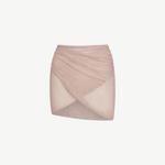 The Lumiere Skirt is a light pink, textured knit mini skirt with a criss-cross, wrap-style front and subtle sparkle details, featuring sequin bead accents for added shimmer, isolated on a white background.