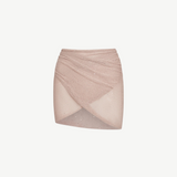 The Lumiere Skirt is a light pink, textured knit mini skirt with a criss-cross, wrap-style front and subtle sparkle details, featuring sequin bead accents for added shimmer, isolated on a white background.