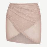 The Lumiere Skirt is a light pink, textured knit mini skirt with a criss-cross, wrap-style front and subtle sparkle details, featuring sequin bead accents for added shimmer, isolated on a white background.