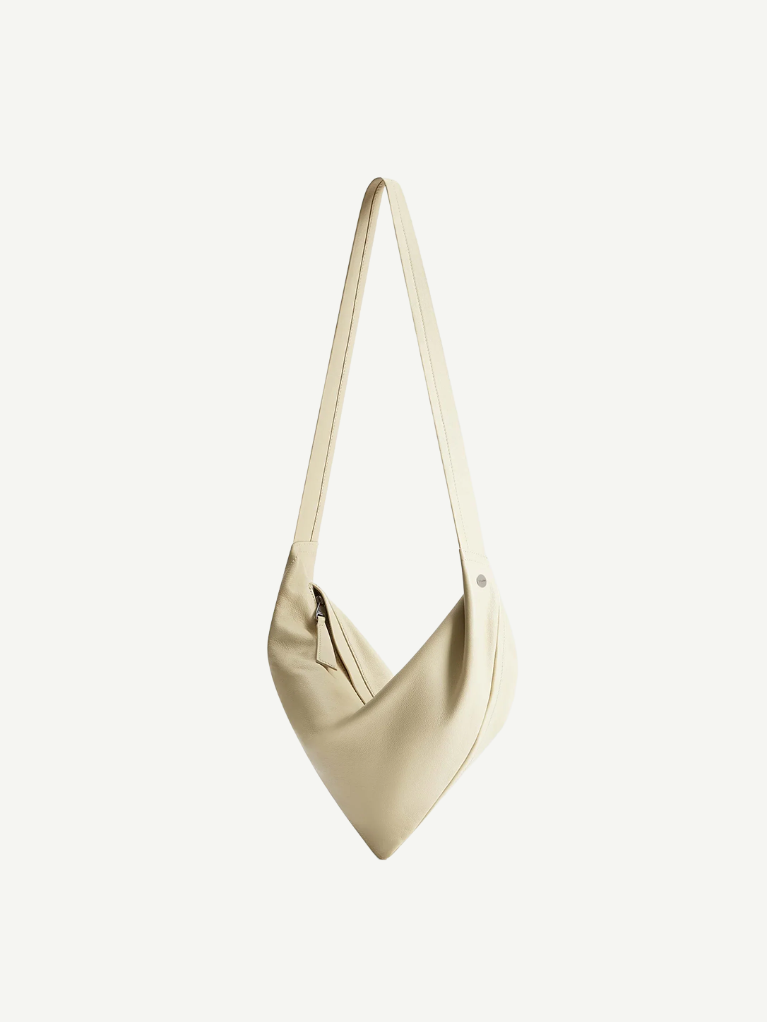 Introducing the Vancouver Sling Bag: a minimalist cream-colored sculptural shoulder bag with a single long strap, crafted from smooth, soft nappa leather and showcasing a subtle angled design, photographed on a plain white background.