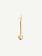 The Heart Bag Charm features a shiny, puffy heart pendant hanging from a 14KT gold plated chain, adding timeless elegance to any accessory. Shown on a plain white background, this piece channels the chic style of a Martha Calvo pendant.