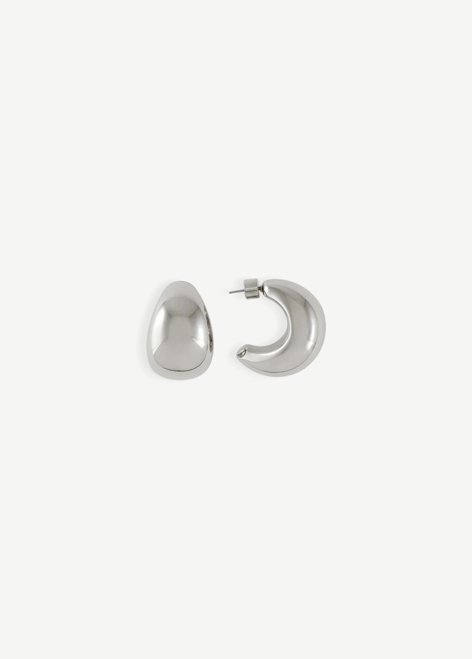 A pair of Jordyn Hoops in Rhodium—shiny, crescent-shaped stud earrings with pierced backs—are displayed against a plain white background, with one earring showing the front view and the other displaying the side profile.