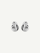 The Rhodium Amina Earrings are featured on a plain white background, showcasing an intricate interwoven knot design with a polished, shiny finish and a secure pierced back.