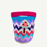 Introducing the Champinones Bag: a vibrant, handmade crocheted basket with a zigzag pattern in pink, blue, purple, and white. Expertly crafted from crochet wool, it features an adorable applique of a pink mushroom with a brown stem on the front. This unique piece infuses any space with playful charm and artistic flair.