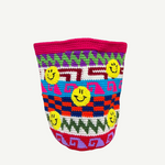 The Smileys Bag is a colorful crochet wool bag featuring geometric patterns in red, blue, purple, green, and pink, adorned with multiple yellow smiley faces on a white background. This unique handmade accessory brings a cheerful touch to any outfit.
