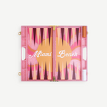 Introducing the Miami Backgammon Board Game: a chic pink acrylic set showcasing “Miami Beach” in elegant white script atop a lively orange, pink, and maroon playing surface. With dedicated compartments on each side for game pieces and dice, this Miami backgammon board is an ideal addition to any gift box.