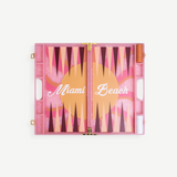Introducing the Miami Backgammon Board Game: a chic pink acrylic set showcasing “Miami Beach” in elegant white script atop a lively orange, pink, and maroon playing surface. With dedicated compartments on each side for game pieces and dice, this Miami backgammon board is an ideal addition to any gift box.