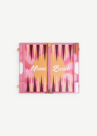 Introducing the Miami Backgammon Board Game: a chic pink acrylic set showcasing “Miami Beach” in elegant white script atop a lively orange, pink, and maroon playing surface. With dedicated compartments on each side for game pieces and dice, this Miami backgammon board is an ideal addition to any gift box.