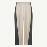 Beige Zoela Pants featuring black side panels, an elastic waistband, and a relaxed, wide barrel-leg silhouette, showcased against a plain white background.