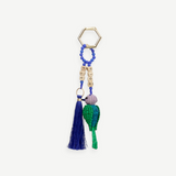 The Hummingbird Keychain features a gold hexagonal ring, blue beads, cube letter beads, a blue tassel, and a green woven chili pepper charm—each element reflecting exquisite Colombian craftsmanship in every detail.