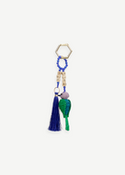 The Hummingbird Keychain features a gold hexagonal ring, blue beads, cube letter beads, a blue tassel, and a green woven chili pepper charm—each element reflecting exquisite Colombian craftsmanship in every detail.