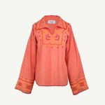 The Poppy Shirt is a long-sleeve, coral-colored silk blouse adorned with yellow and pink embroidered patterns on the chest, cuffs, and collar. This elegant embroidered shirt features slightly flared sleeves and a split neckline. For best care, it is dry clean only.