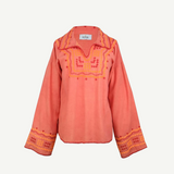 The Poppy Shirt is a long-sleeve, coral-colored silk blouse adorned with yellow and pink embroidered patterns on the chest, cuffs, and collar. This elegant embroidered shirt features slightly flared sleeves and a split neckline. For best care, it is dry clean only.