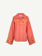 The Poppy Shirt is a long-sleeve, coral-colored silk blouse adorned with yellow and pink embroidered patterns on the chest, cuffs, and collar. This elegant embroidered shirt features slightly flared sleeves and a split neckline. For best care, it is dry clean only.