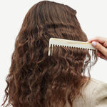 Person combing wavy hair with a white comb on a neutral background