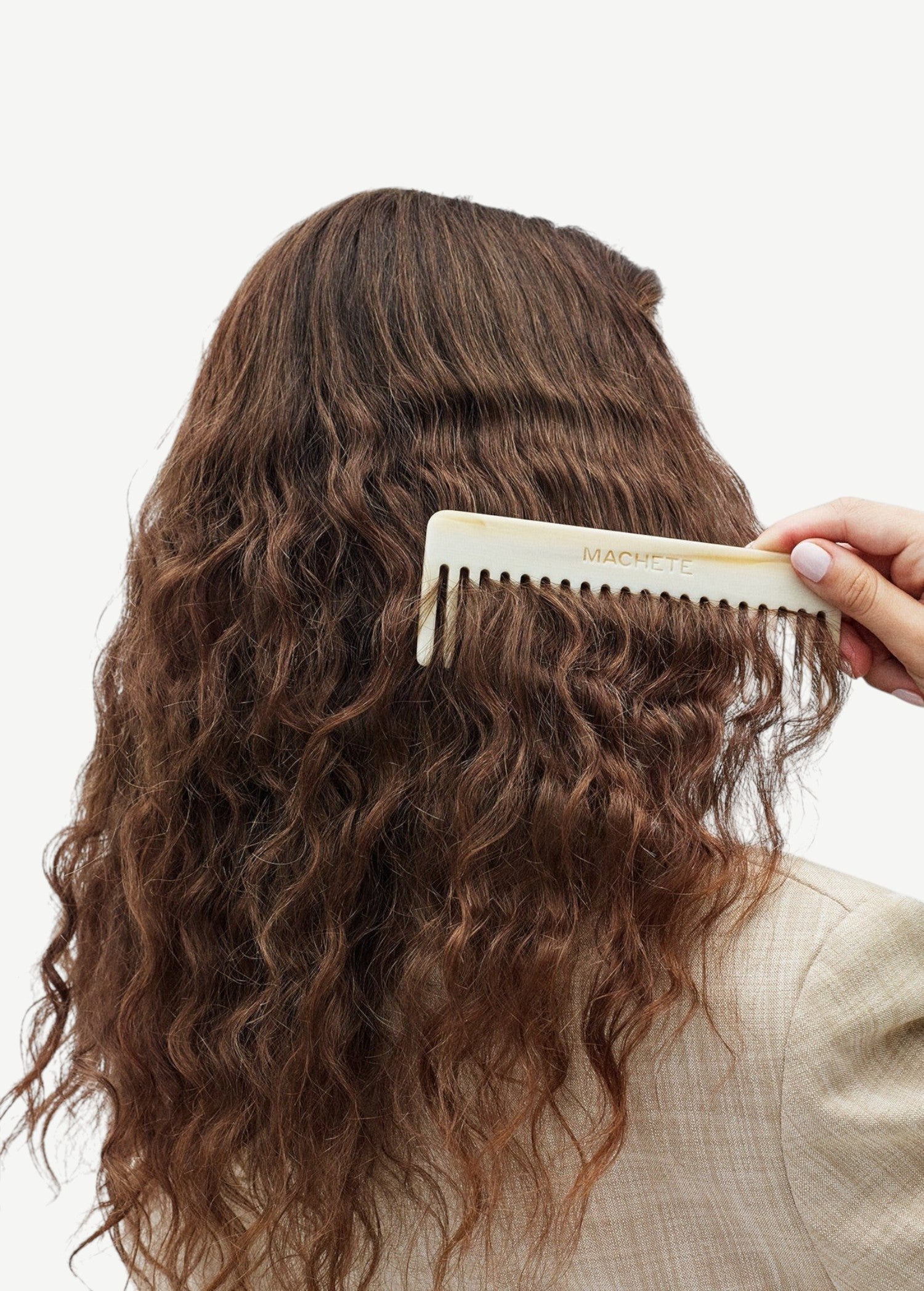 A hand uses a light-colored, Italian acetate No. 2 Comb on wavy brown hair.