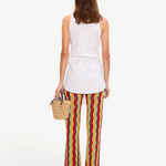 A person from the back wearing a white sleeveless top and Ophelia Knit Pant flared crochet pants with a colorful vertical chevron pattern, holding a small straw handbag.