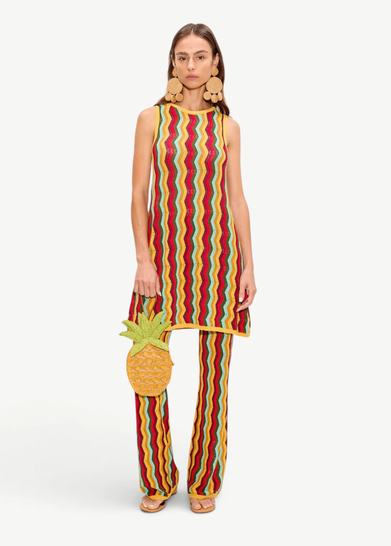 A person wearing a sleeveless knit tunic and matching Ophelia Knit Pant in a colorful vertical chevron pattern, carrying a pineapple-shaped handbag.