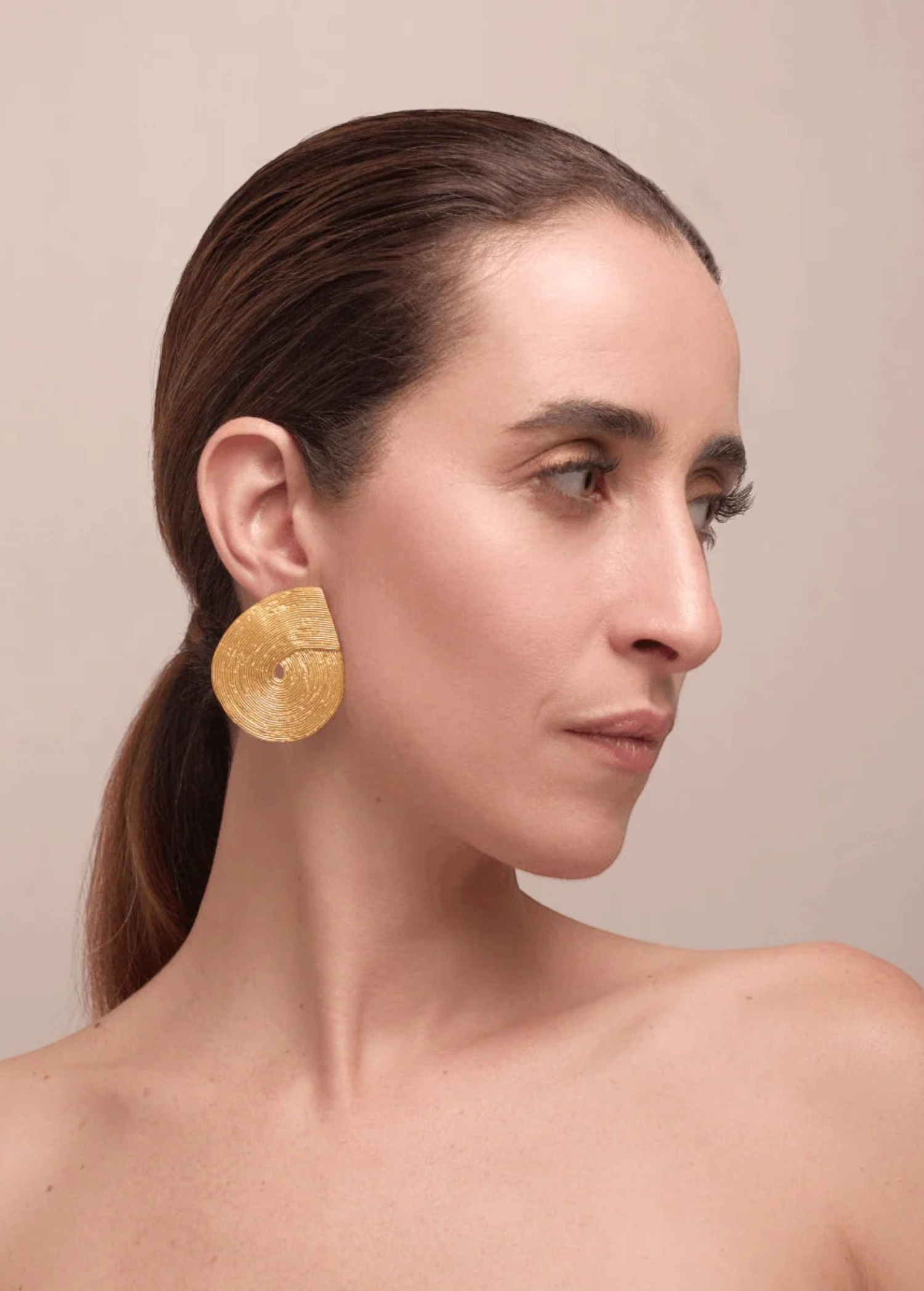KABE SHOP INC Wixa earrings featuring a gold-toned, sculptural spiral design worn by a woman in profile.