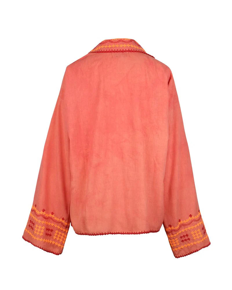 Back view of the Poppy Shirt, a coral pink embroidered jacket featuring wide sleeves, orange and yellow geometric embroidery on the cuffs, and matching trim along the edges. Dry clean only.