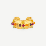 Introducing the Theodora Cuff: a wide gold ring with a gently pointed front, this handcrafted piece is adorned with small, colorful round gemstones—including red, green, purple, and orange—set against a simple white backdrop. Effortlessly wearable, the Theodora Cuff brings vibrant elegance to any ensemble.