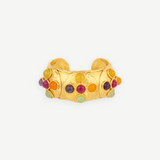 Introducing the Theodora Cuff: a wide gold ring with a gently pointed front, this handcrafted piece is adorned with small, colorful round gemstones—including red, green, purple, and orange—set against a simple white backdrop. Effortlessly wearable, the Theodora Cuff brings vibrant elegance to any ensemble.