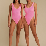 Two models wearing KABE SHOP INC Ruby one-piece swimsuits in bright pink with a textured fabric and high-cut design.