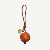 KABE SHOP INC peach-shaped wooden bag charm with a braided brown leather strap and a gold-tone metal logo tag.