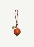 KABE SHOP INC peach-shaped wooden bag charm with a braided brown leather strap and a gold-tone metal logo tag.