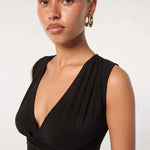 A woman with slicked-back hair wears gold hoop earrings and the Sunnery Top—a sleeveless black Tencel jersey V-neck style—standing against a plain light background.