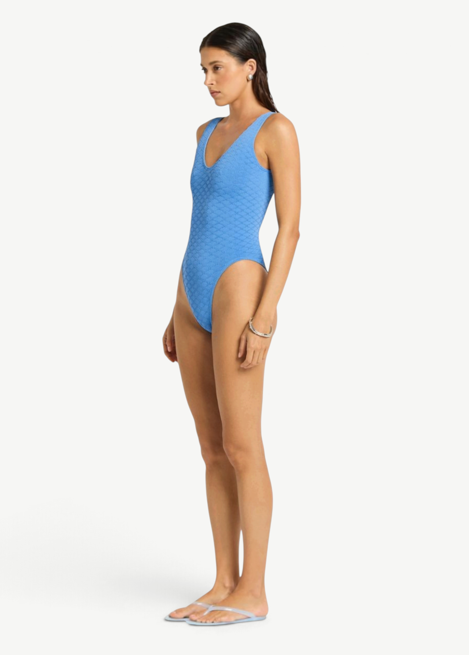 KABE SHOP INC Mara blue textured one-piece swimsuit with V-neckline and high-cut leg worn by a model, side view