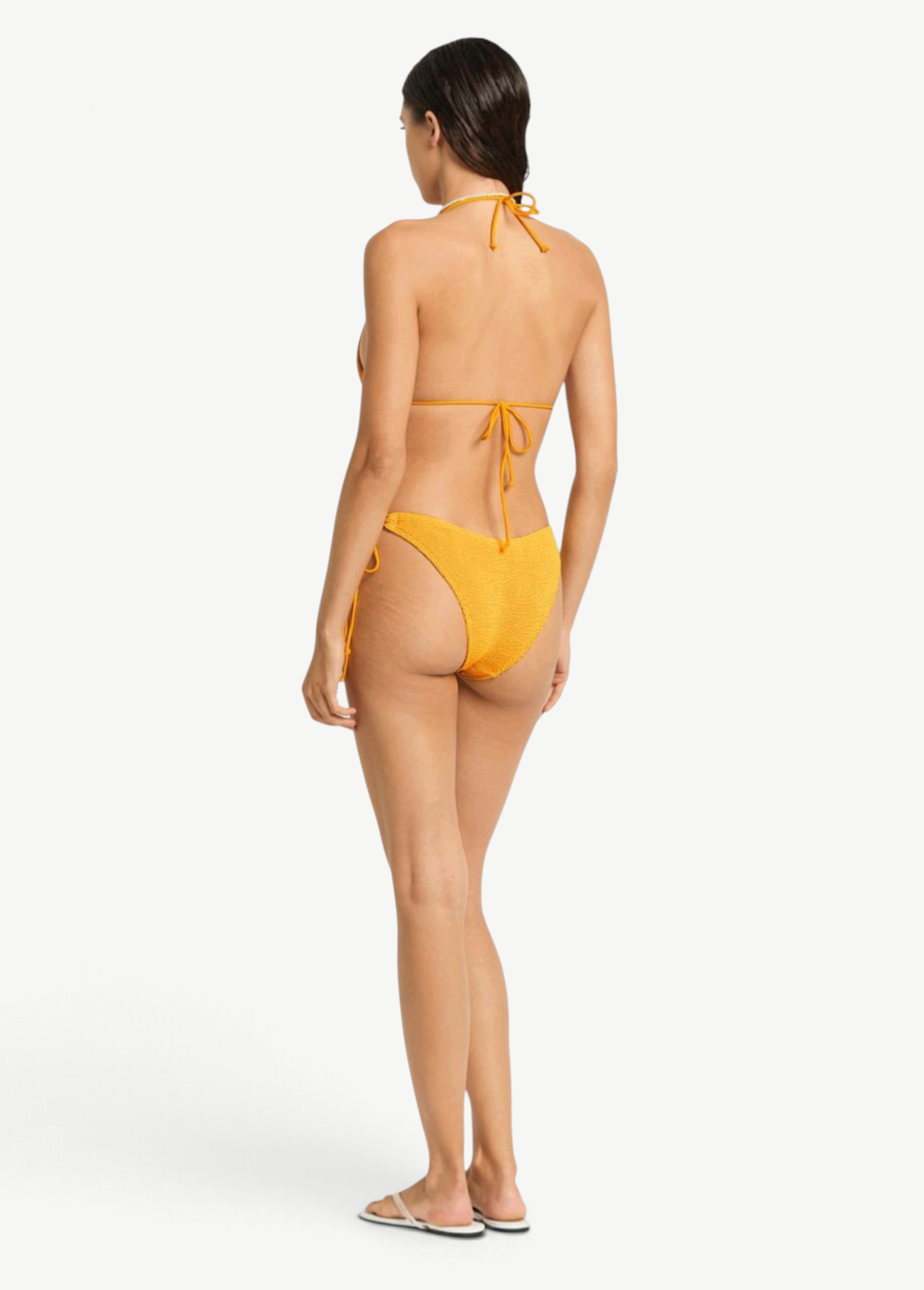Model wearing KABE SHOP INC yellow textured Sonali bikini briefs with side loop ties, back view.