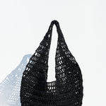 The Market Net Bag, a black, woven crochet-style handbag with a single looped handle, sits on a light wooden surface against a plain white background.