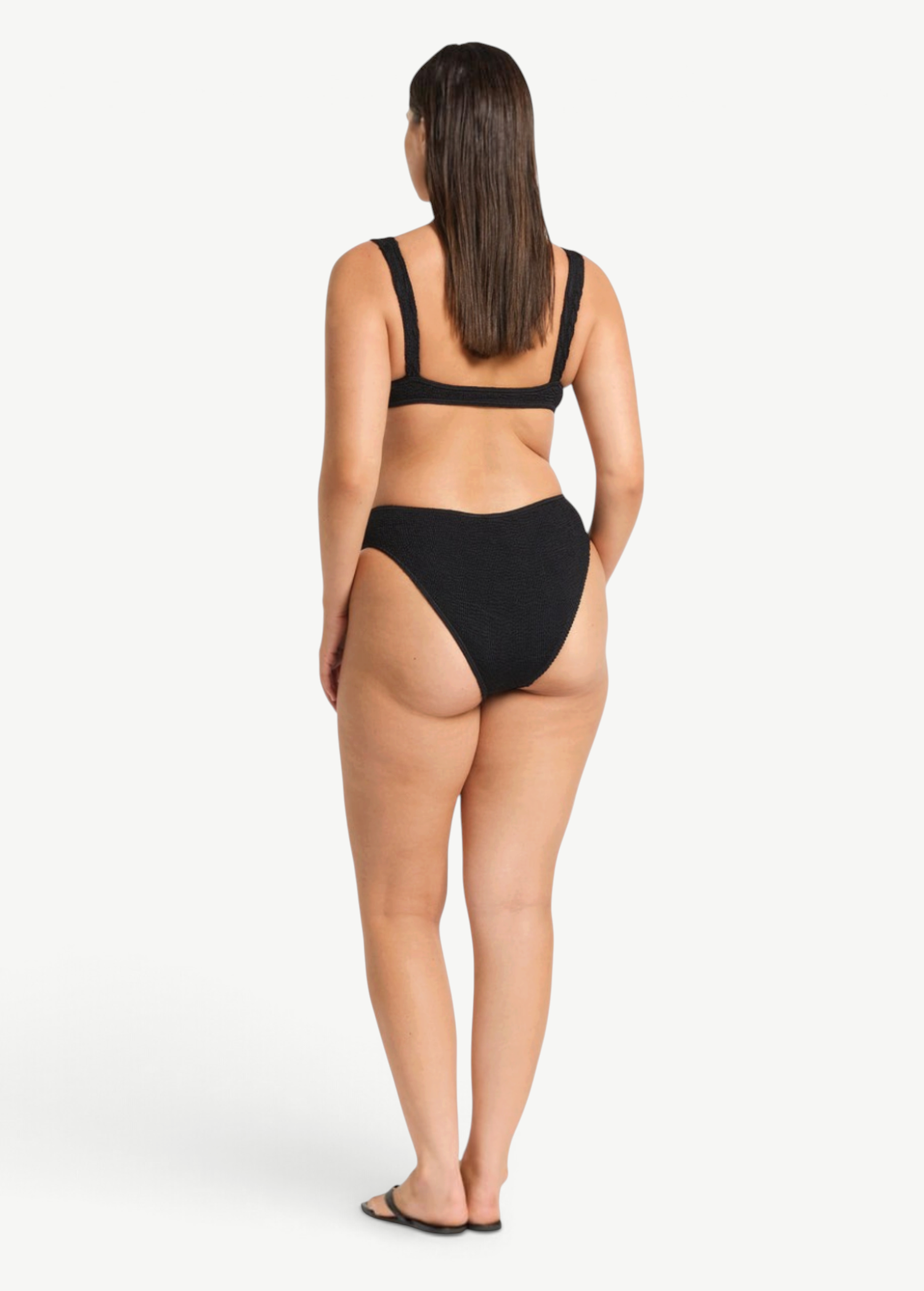 Model wearing KABE SHOP INC Olivia black high-cut bikini brief in shimmer crinkle fabric, back view.