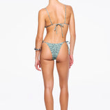 A woman stands facing away, wearing a light green patterned recycled nylon swimwear bikini and sandals, with her hair tied back. The bikini features beaded tie side straps on both the top and the zebra sage Praia Bottom. The background is plain white.
