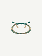 The N° 183 Braided Bracelet is a green and gold friendship bracelet with adjustable ties and gold tassel accents, featuring a yellow gold finish, displayed on a white background.