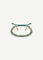 The N° 183 Braided Bracelet is a green and gold friendship bracelet with adjustable ties and gold tassel accents, featuring a yellow gold finish, displayed on a white background.