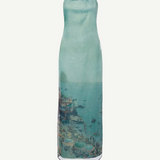 Strapless, floor-length Amara Dress in a sheer, light blue fabric featuring a scenic coastal print of a beach and town, perfect for special occasions.