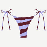Introducing the Praia Bottom: a bikini bottom with maroon and light purple diagonal stripes, featuring adjustable side ties with bows on both hips, crafted from our eco-friendly Peach Perfect swimwear fabric.